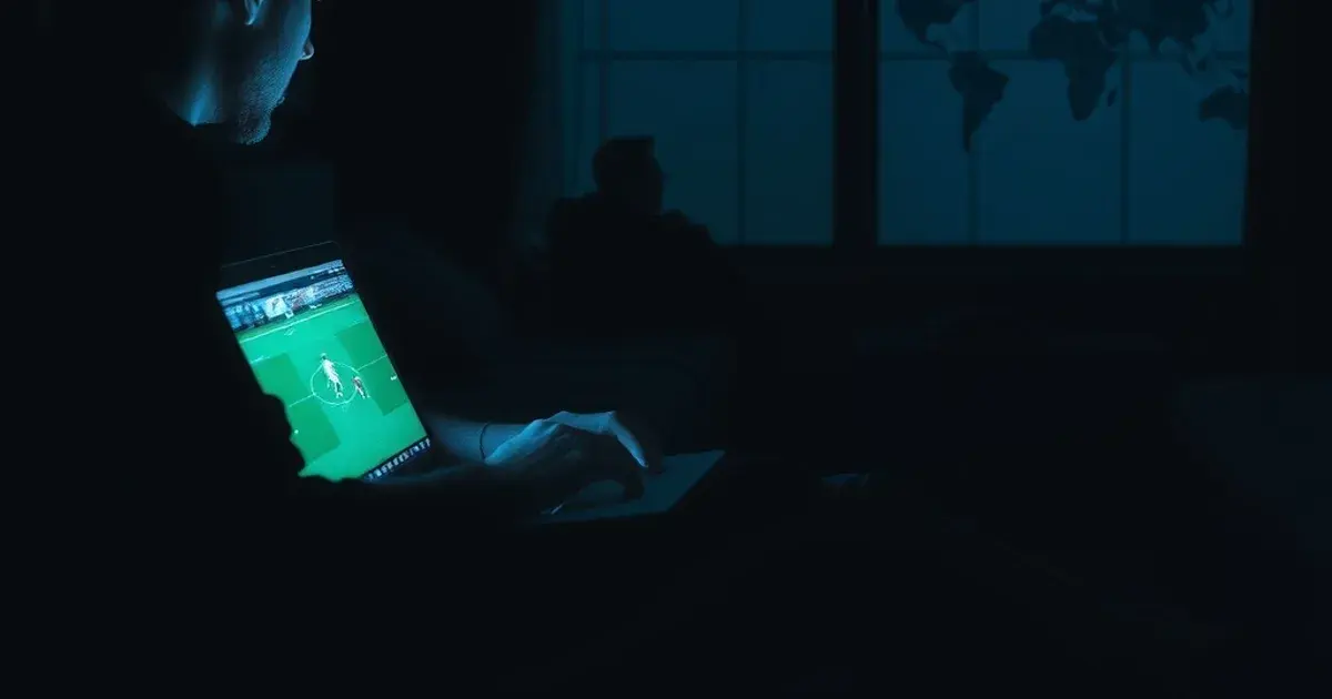 Iemand kijkt 's avonds in een hotelkamer in het buitenland naar een livestream van een voetbalwedstrijd op een laptop